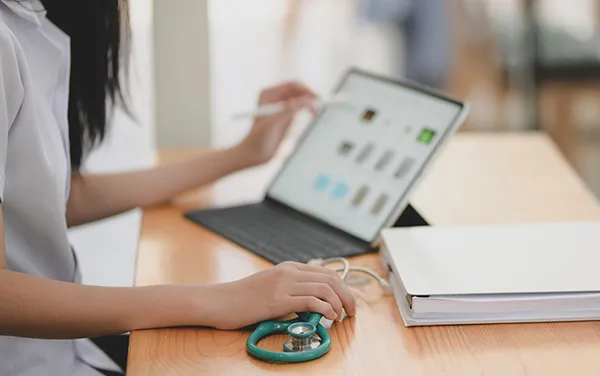 A woman holding a stethoscope while working on a laptop computer.